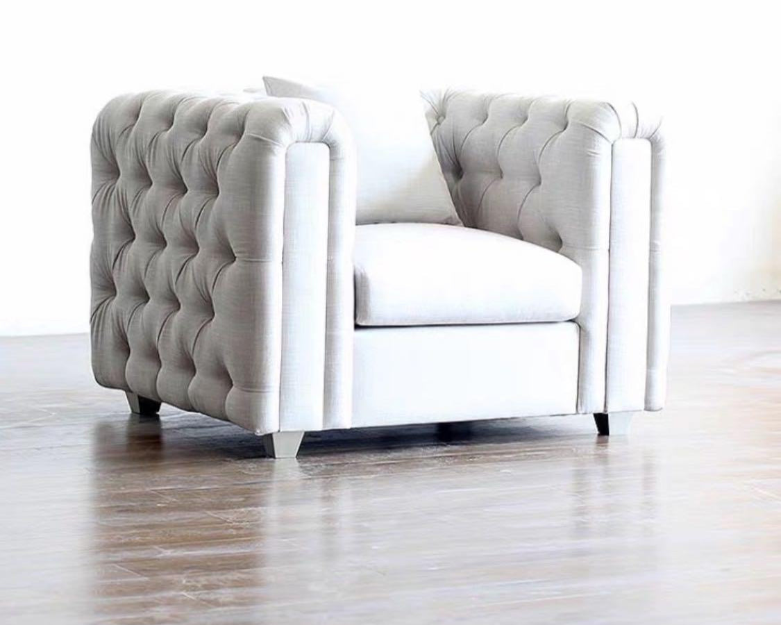 A tufted Chesterfield chair with beige upholstery and deep button tufting, standing on a hardwood floor.