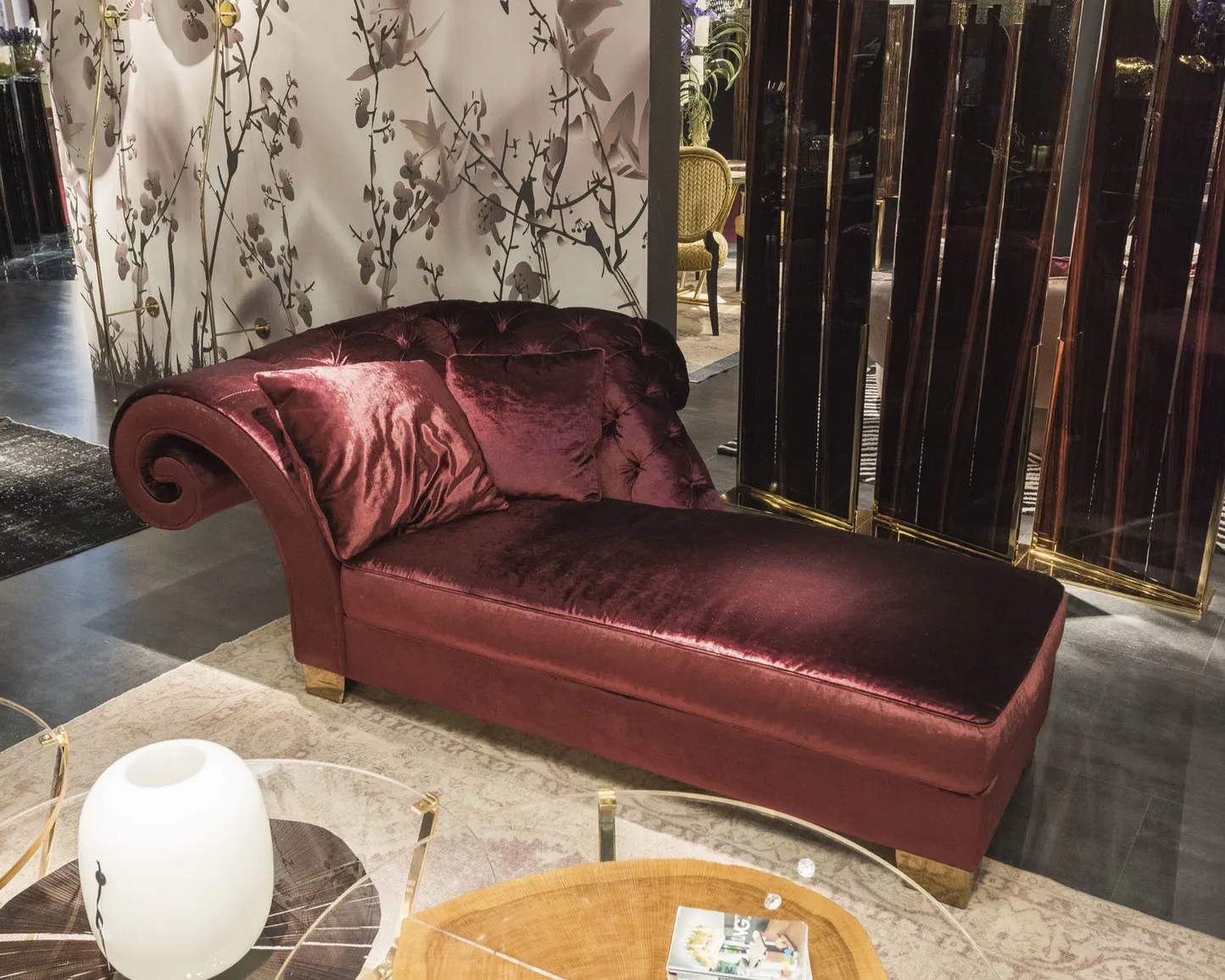 Maroon velvet chaise lounge in a stylish room with decorative elements.