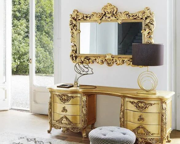 Gold ornate desk with matching mirror and lamp in a room with large windows.