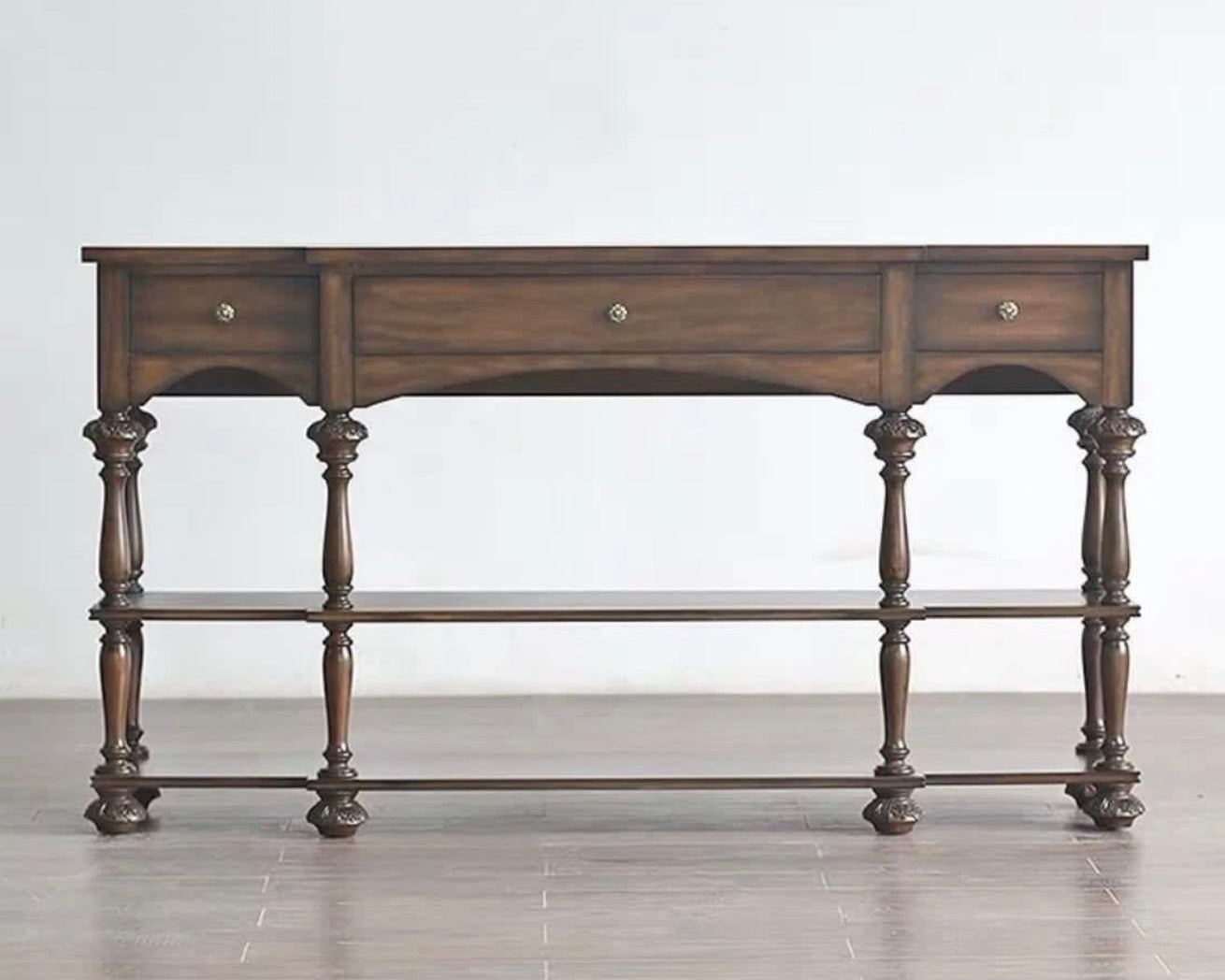 Wooden console table with three drawers on a plain background