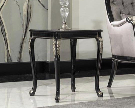 A classic baroque design side table with a sleek lacquer finish, featuring intricate carved details, placed on a polished floor next to an elegant chair with a decorative wall in the background.