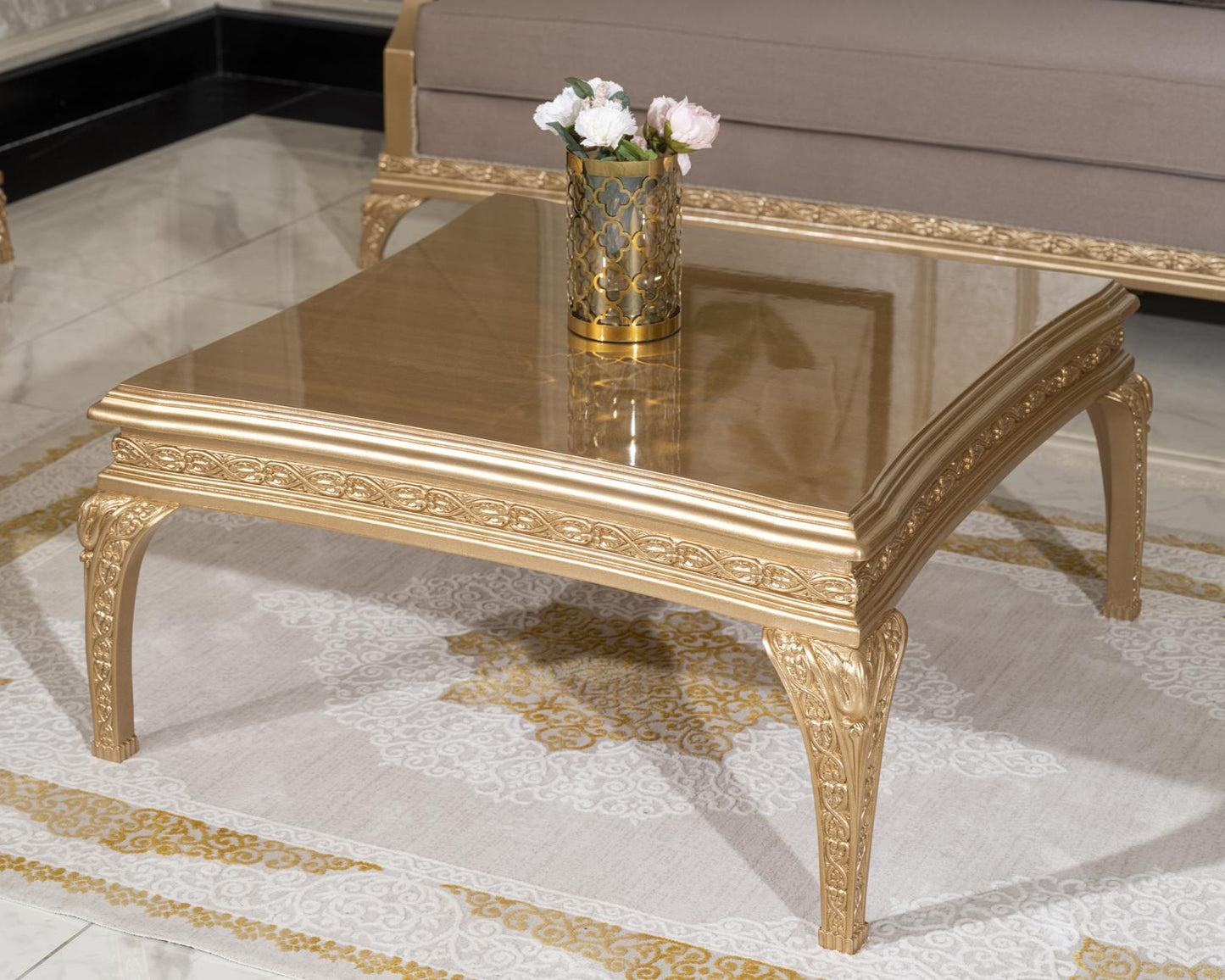 An elegant mahogany wood coffee table with a glossy finish, featuring intricate detailing and a floral arrangement on top, placed on a luxurious carpet.