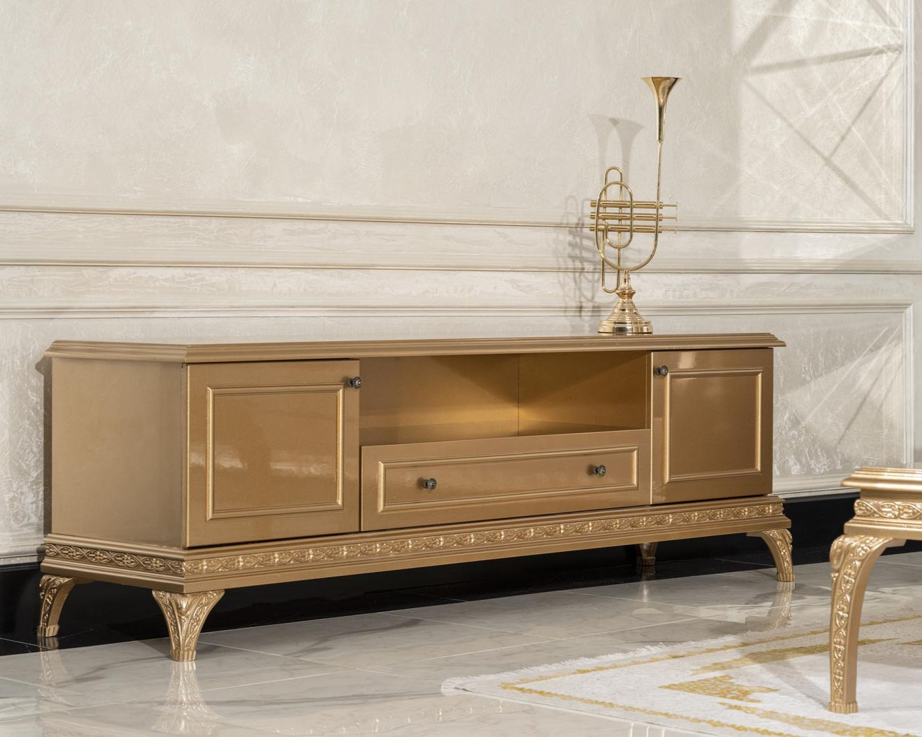 An elegant golden Rococo style TV console cabinet with intricate wood carvings and legs, placed in a luxurious interior setting.
