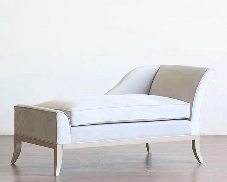 A modern chaise lounge with a beige upholstery, gold detailing, and a wooden frame.