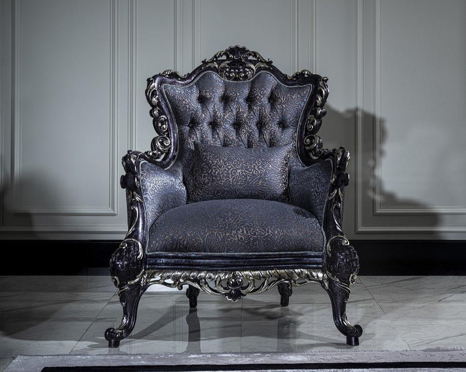 A luxurious French armchair with carved details in a mahogany wood frame and upholstered in a jacquard fabric with a floral pattern. The chair is positioned in a room with a grey wall and a striped rug.