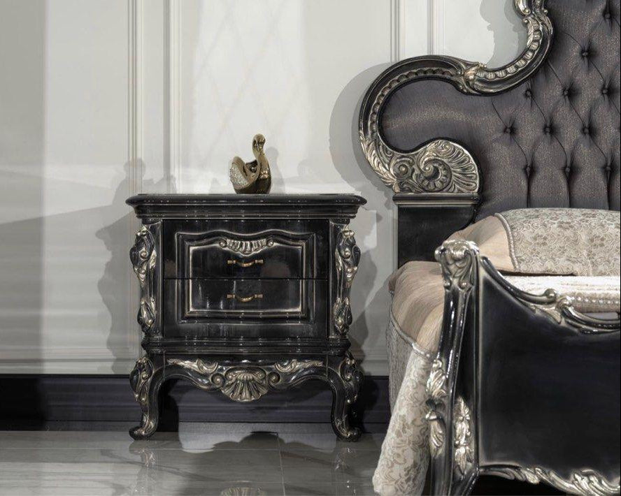 A luxurious baroque-style nightstand with intricate carved details, placed in an elegant room with a mirrored wall and a lavishly upholstered chair.