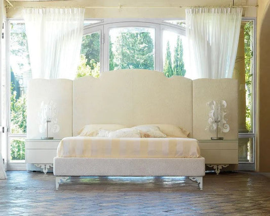 Large white bed in a room with large windows and white curtains