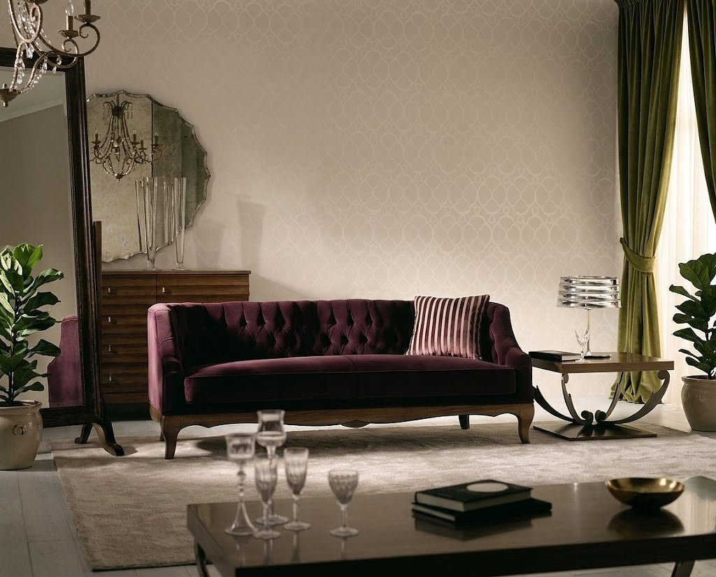 A classic tufted velvet sofa in deep burgundy, styled in a luxurious living room with green curtains, a patterned wall, and a dark wood coffee table in the foreground.