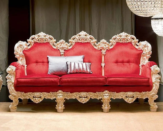 Red sofa with ornate gold frame and decorative pillows in a room with dark curtains and a chandelier.