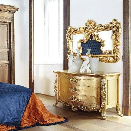 Decorative gold dresser with ornate mirror in a room with wooden floor and white walls.