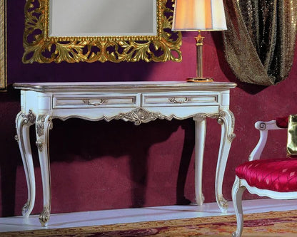 Decorative console table with gold accents in a room with a red wall, gold-framed mirror, and pink chair.