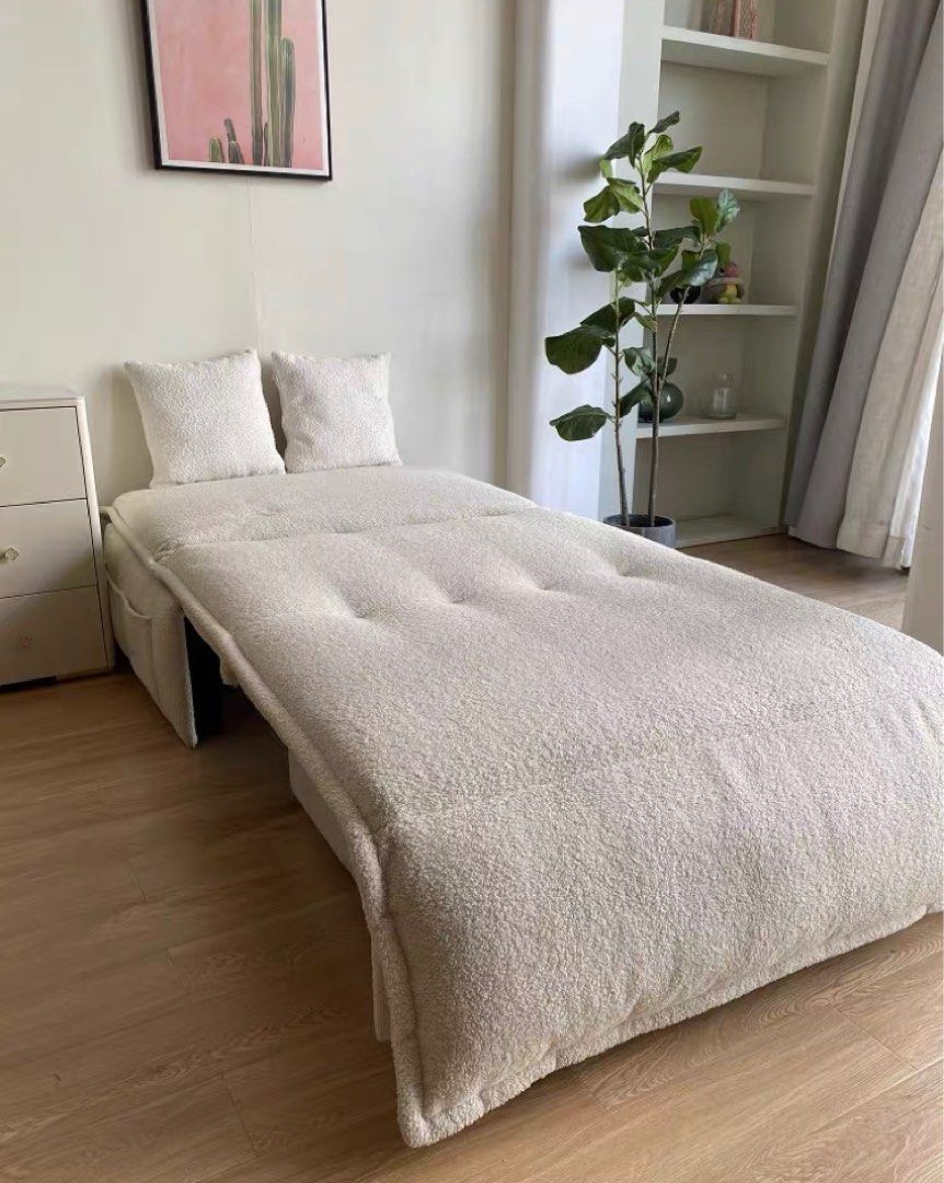 White sofa bed in a room with a plant and shelves.
