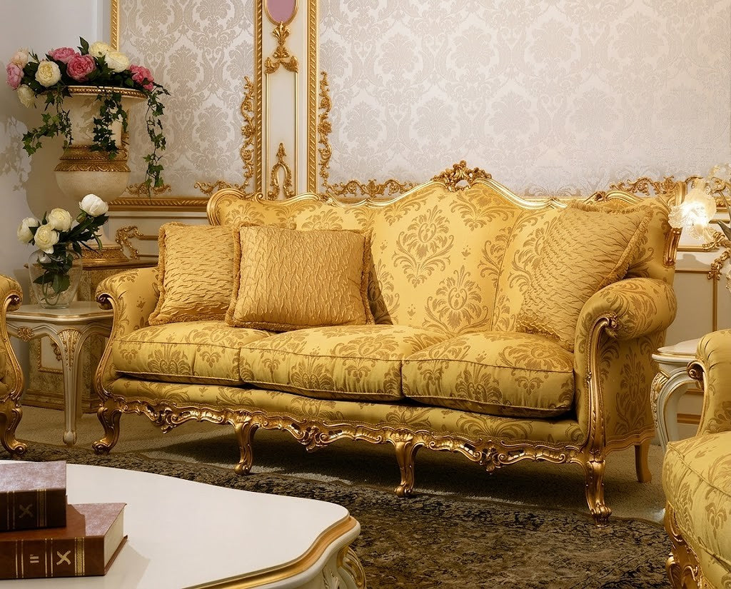 An ornate golden-yellow baroque-style sofa with carved gold frames and matching patterned cushions, set in a decorated room with wallpaper, side tables, and floral arrangements.