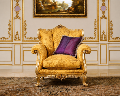 A classic French provincial style armchair upholstered in golden-yellow damask fabric with ornate gold carved wood legs, set against a decorated cream wall with gold paneling and a purple accent pillow.