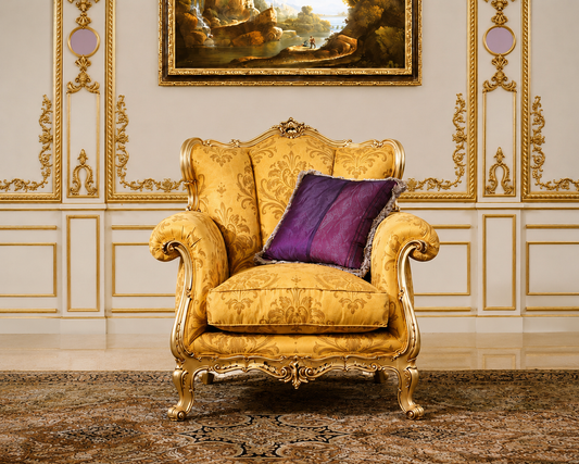 A classic French provincial style armchair upholstered in golden-yellow damask fabric with ornate gold carved wood legs, set against a decorated cream wall with gold paneling and a purple accent pillow.