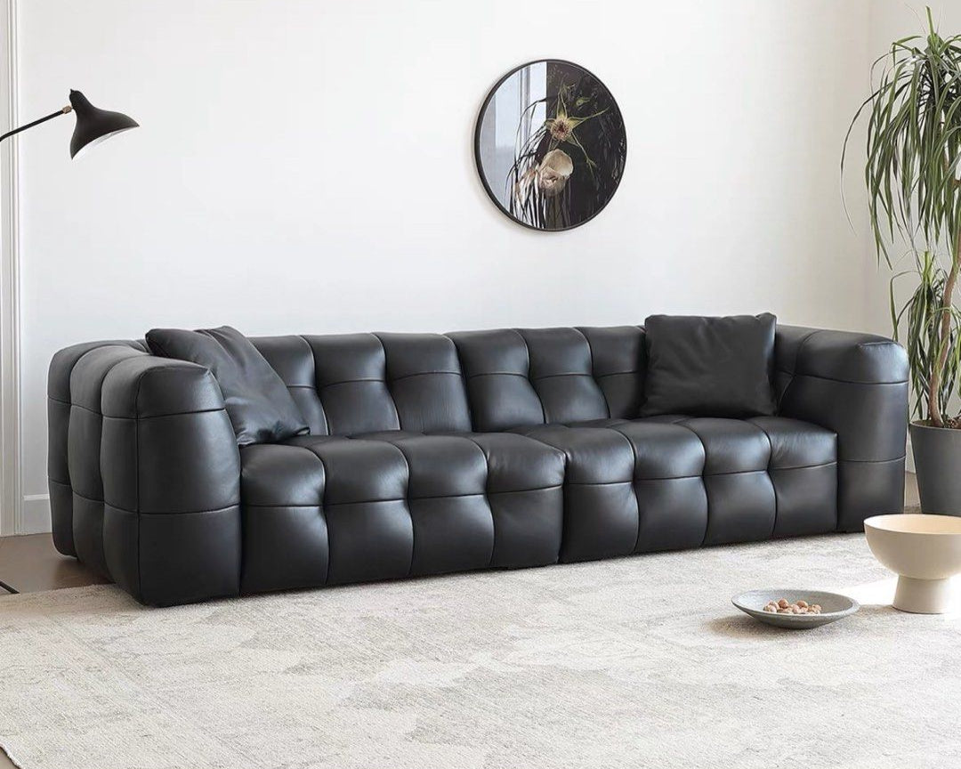 Black leather sofa in a modern living room with a mirror and plant.