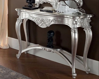 Decorative silver console table with intricate designs against a brown wall.