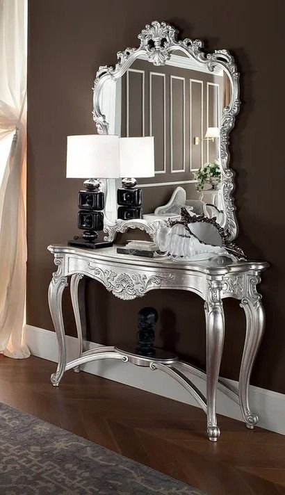 Decorative silver console table with mirror and lamp against a brown wall.