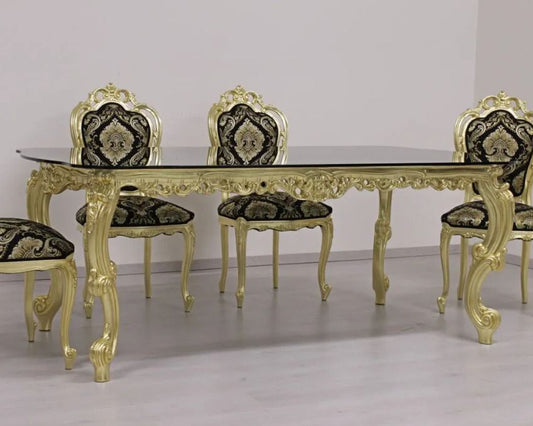 Gold dining table set with ornate chairs against a plain background