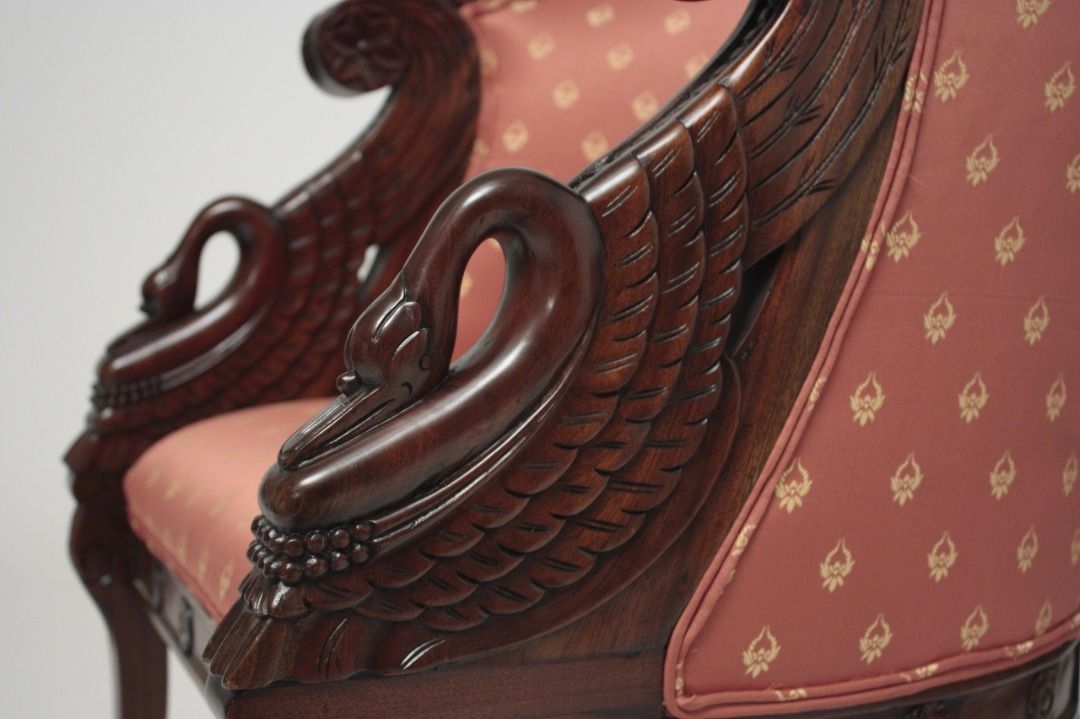 Close-up of an ornate chair with detailed carvings and red fabric with gold patterns.
