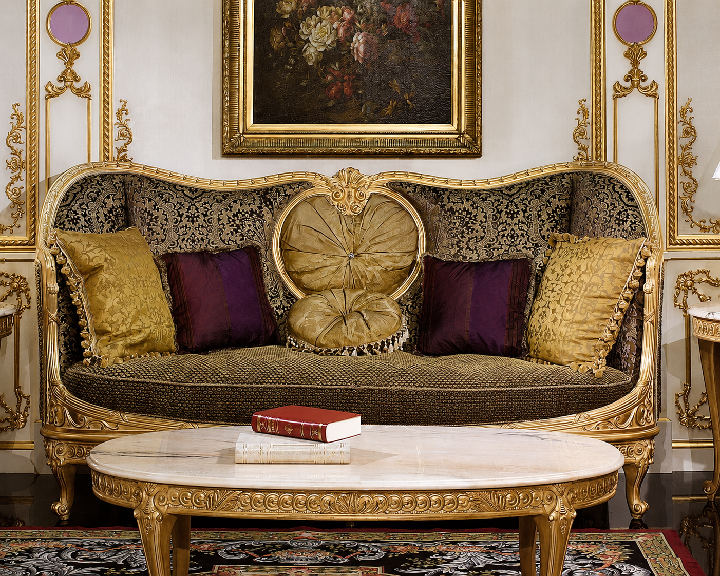 An ornate baroque-style sofa with a gilded frame, patterned upholstery, and decorative pillows, set in a luxurious room with a matching carved coffee table and framed wall art.