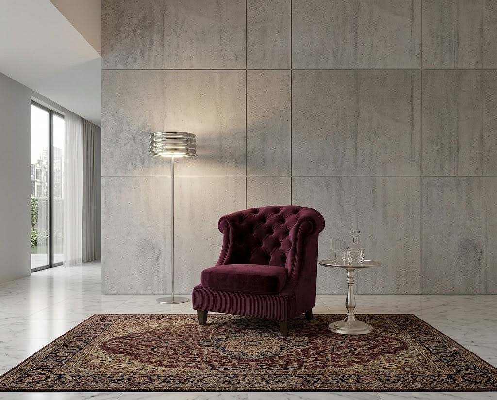 A deep burgundy tufted velvet armchair sits on a patterned area rug in a modern living room with a concrete-paneled wall, a floor lamp, and a small side table.