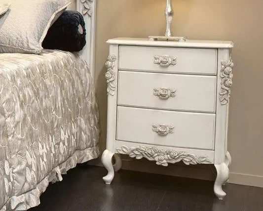 Decorative white nightstand next to a bed with floral headboard