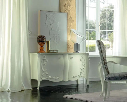 Decorative white console table with intricate carvings in a bright room with large windows.