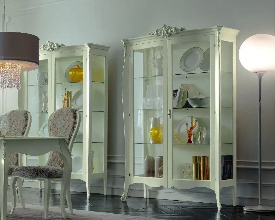 White display cabinets with decorative items in a room with a dining table and chairs.