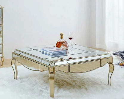 A luxurious coffee table with a mirrored surface and gold finish accents, displayed in a bright room with a white rug.