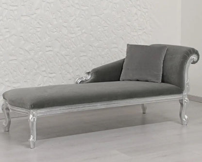 Gray velvet chaise lounge with silver legs against a textured white wall.
