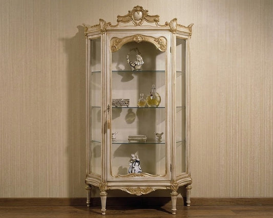 An ornate vintage-style glass display cabinet with a distressed gold and beige frame, shown against a beige textured wall and wooden floor.