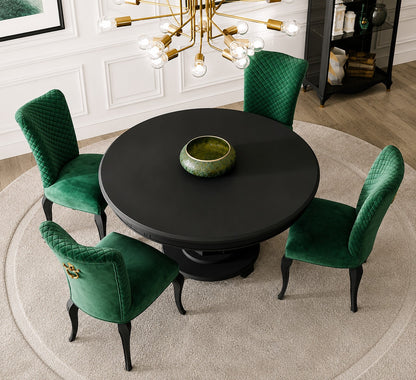 A round black dining table surrounded by four emerald green velvet upholstered chairs with gold-tone hardware, set on a light beige circular rug in a styled dining room.