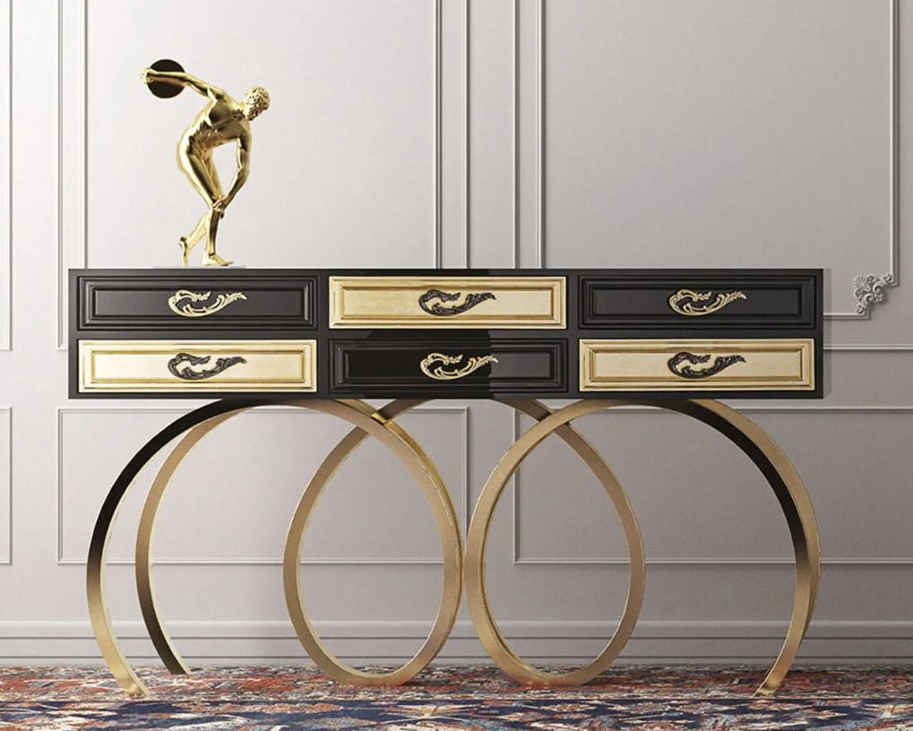 Decorative console table with gold legs and black and gold drawers against a white wall.