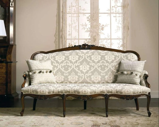 Vintage-style sofa with intricate carvings in a room with a lamp and window.