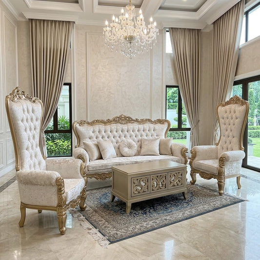 An elegant luxury living room set featuring a tufted cream sofa with ornate gold legs, two matching high-back wingback armchairs, a carved wooden coffee table, and a patterned area rug, set against beige walls with tall drapes and a crystal chandelier.